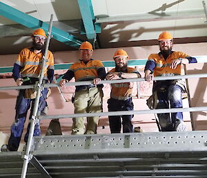 Four expeditioners on mezzanine level looking down at camera smiling