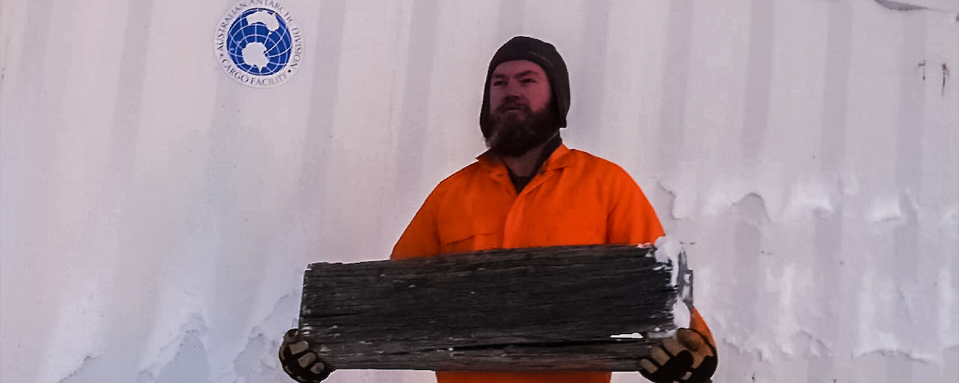 Expeditioner dressed in an orange jumpsuit holding a piece of wood