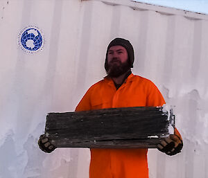 Expeditioner dressed in an orange jumpsuit holding a piece of wood