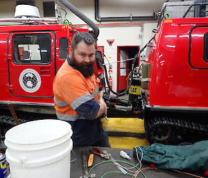 Bearded expeditioner in workshop hiding a handmade gift with a smirk