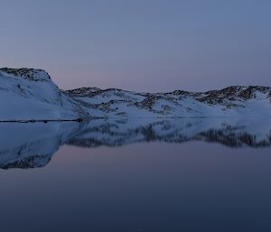 Snow and rock covered hills surrounding the lake and their symmetrical reflection in the water