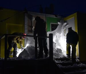 Three expeditioners illuminated by torches dig snow out of the entrance of Platcha Hut