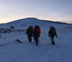 Three expeditioners walking back towards the yellow tracked vehicle beside a snow capped hill