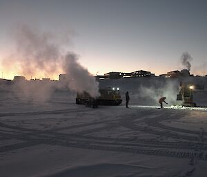 Diesel mechanics working on the sea ice hole in foreground in background the station is silhouetted.