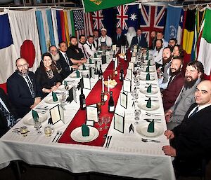 Pre-dinner photo of the expedition team seated at the midwinter dinner. Everyone is dressed up and surrounded by all the flags of the Antarctic Treaty nations.