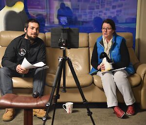 Two expeditioners facing the camera lean into wards an ipad on which a videoconference is being conducted with schoolchildren