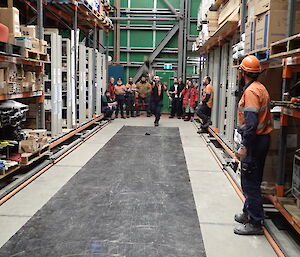 Expeditioner in mid-throw of a boot down an aisle in the warehouse with crowd in background