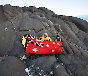 Three expeditioners holding a flag facing the camera