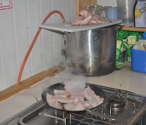 Bacon being cooked on a frying pan in a field hut