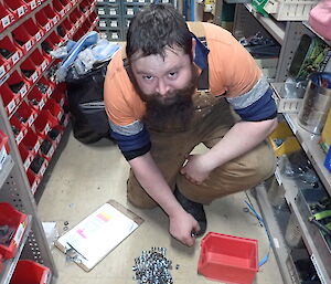 Expeditioner kneeling beside a carton of nuts and bolts