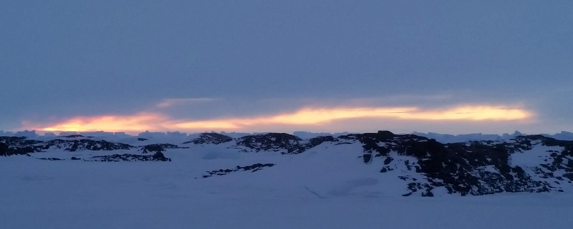 Sunlight filtering through an overcast horizon with icebergs silhouetted