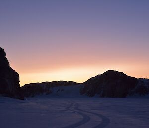 Sunlight silhouetting rock ridgelines and illuminating sea ice