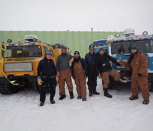 Six expeditioners standing front of two haggs