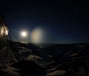 Hut in foreground on left bathed in moonlight illuminating rocks and snow in landscape