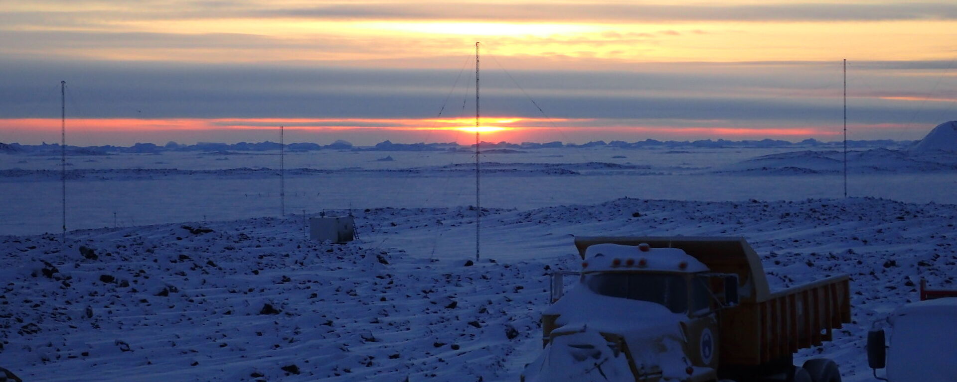 Parked trucks in foreground with sun rising low over the horizon in background