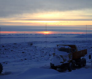 Parked trucks in foreground with sun rising low over the horizon in background