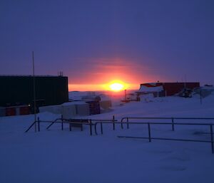 Sun rising on the horizon between two buildings silhouetted in foreground