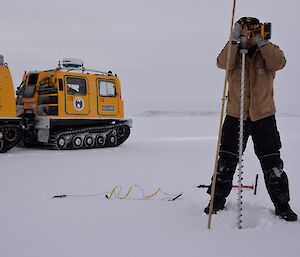 Expeditioner with a handheld drill beginning to drill into the sea ice