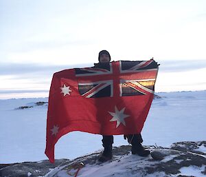 Expeditioner standing beside a cairn holding the red ensign