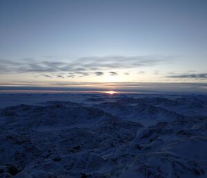 Sea ice and icebergs silhouetted against rising sun on horizon