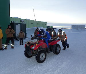 Expeditioner seated on a quad being pushed down a track by several other expeditioners