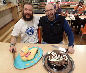 Two expeditioners holding large knives pose behind their cakes