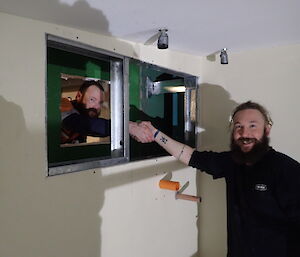 Expeditioners shake hands through a hole in an insulating wall