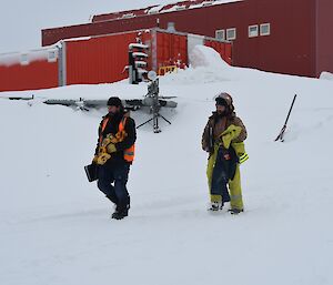 Two expeditioners in fire fighting equipment walk down through the snow outside after completing their training