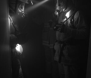 Expeditioners in dark corridor in breathing apparatus checking their air gauges
