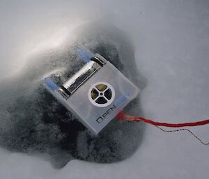 An underwater remotely operated vehicle roughly the size of a shoebox being lowered into the ice hole