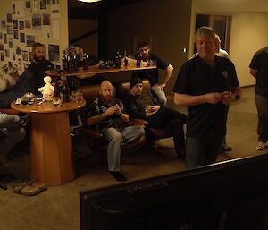 A group of expeditioners at a bar sitting watching a television screen