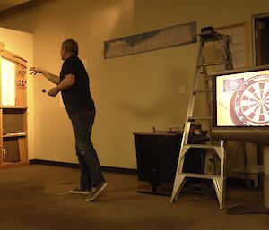 Expeditioner throws a dart at a board with a television screen showing the opposing sides board in the foreground