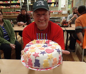 Expeditioner facing camera seated behind a table with birthday cake on it