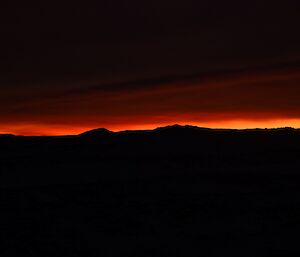 Hills silhouetted against a dark red horizon at sunrise