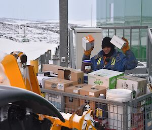 Expeditioner holding 2 minute soup boxes from behind a cage pallet with food supplies.