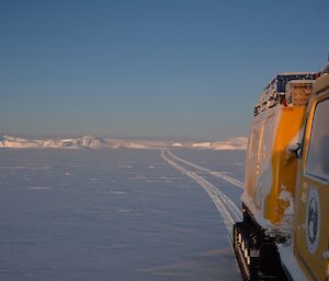 View of side of Hägglunds vehicle with tracks across the sea ice and icebergs in the background.