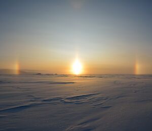 Sun shining above sea ice with symmetrical rainbows at either side.
