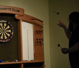 Expeditioner silhouetted against a dartboard, with a dart in mid-flight.