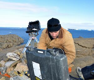 Expeditioner leaning over camera equipment on a rocky outcrop.