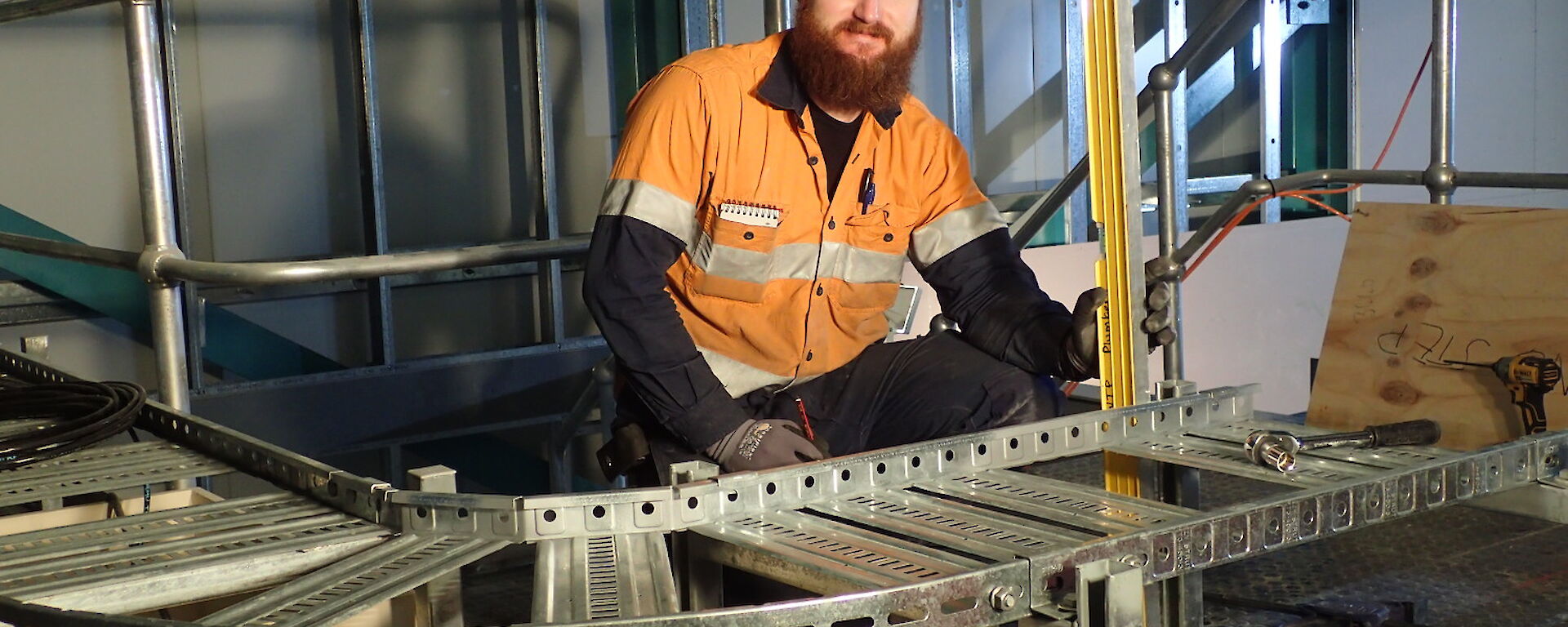Expeditioner kneeling behind a metal brace for electrical wiring.