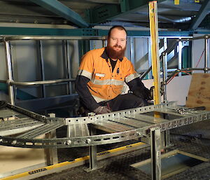 Expeditioner kneeling behind a metal brace for electrical wiring.