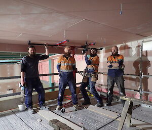 Four expeditioners posing under a ceiling on the mezzanine level of the wastewater treatment facility.