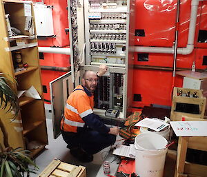 Expeditioner kneeling beside a large switchboard.