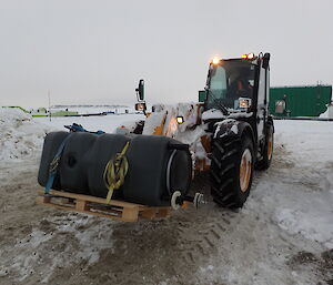 JCB mechanical digger transporting a pallet with a holding tank fastened to it.