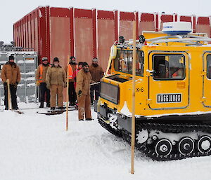 Expeditioners watch as the driver of a yellow Hägglunds tracked vehicle is given the ‘go’ signal.