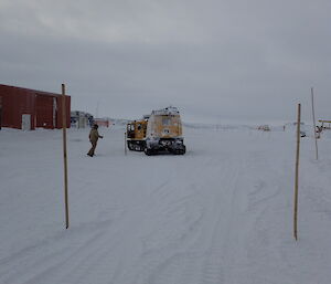 Expeditioner guiding the driver of a yellow Hägglunds tracked vehicle through a slalom course.