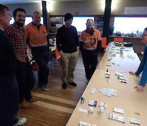 Expeditioners standing beside a table with a range of medical items arranged for first aid kit training.