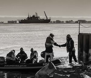 Expeditioners on a small watercraft bid farewell to those staying behind, before heading out to the icebreaker in the distance.