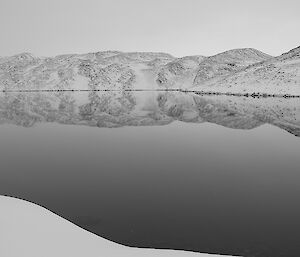 A still lake surrounded by snow-covered hills.