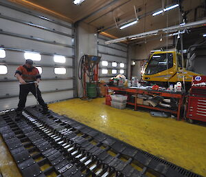 Expeditioner standing on the tracks of a snow groomer, checking the tension of fastening bolts.